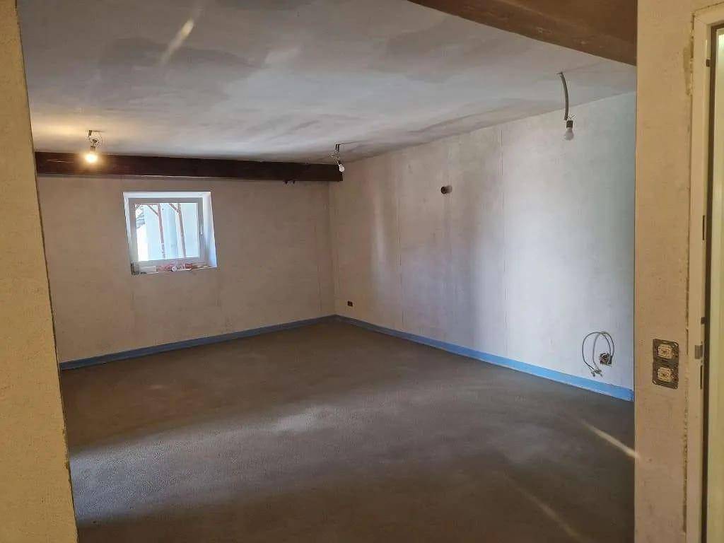 Unfertiger Innenraum mit sichtbaren Holzbalken an der Decke und einem kleinen Fenster.