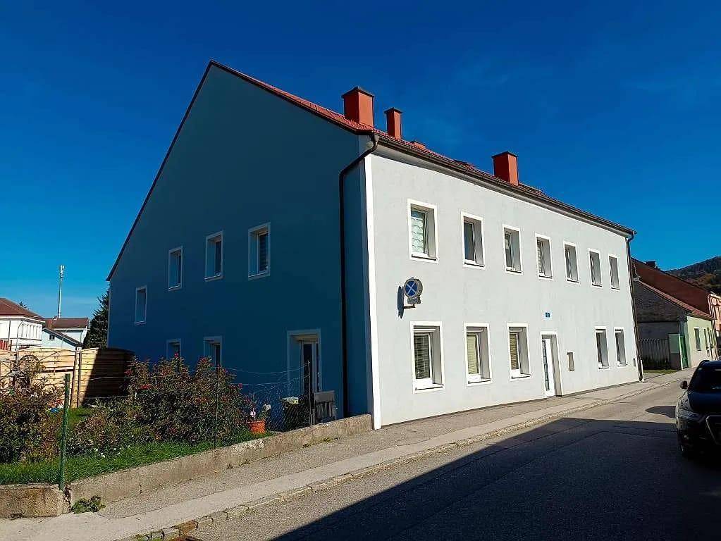 Seitenansicht eines Gebäudes mit hellblauer Fassade, rotem Dach und mehreren Fenstern.