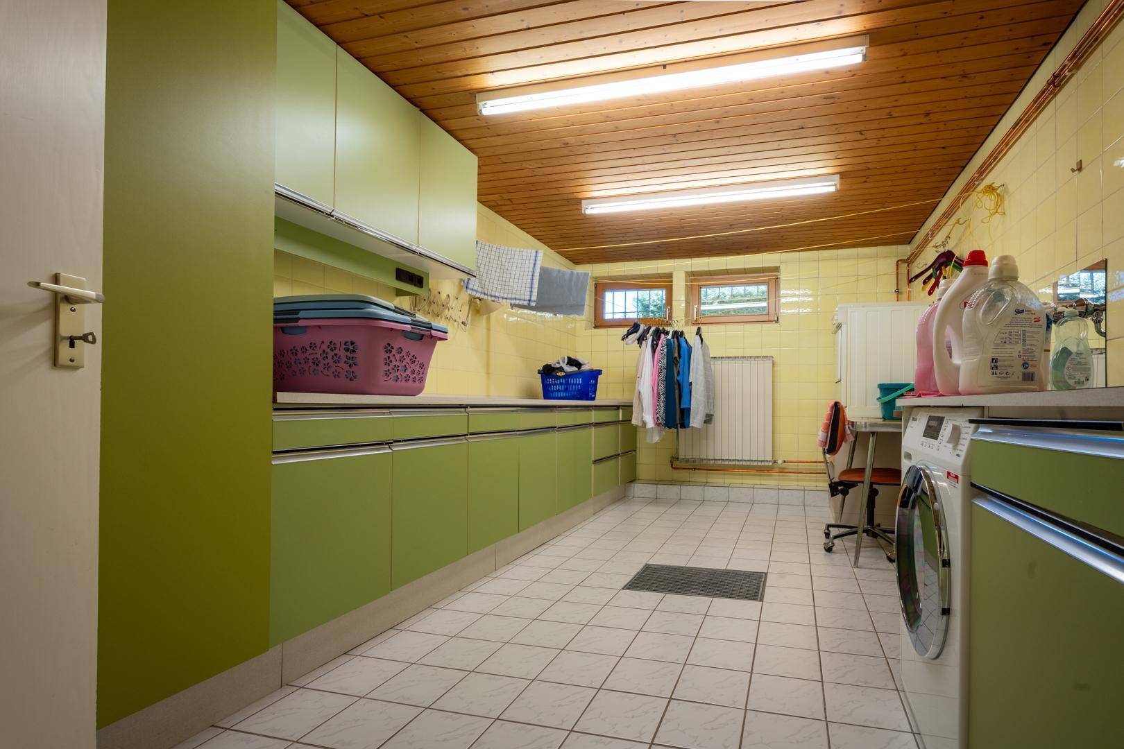 Praktischer Hauswirtschaftsraum mit Waschmaschine, Trockner und viel Stauraum in grünen Schränken.