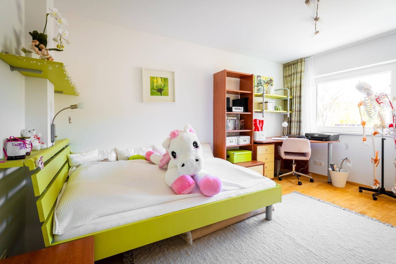 Helles Kinderzimmer mit Einzelbett, Schreibtisch und bunten Dekorationen, ideal für junge Bewohner.