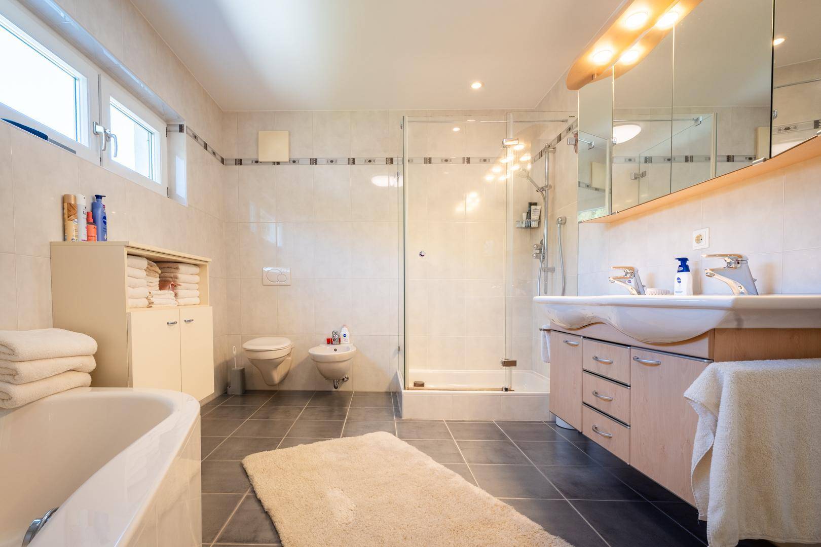Geräumiges Badezimmer mit Badewanne, großer Dusche, Doppelwaschbecken und Fenster.