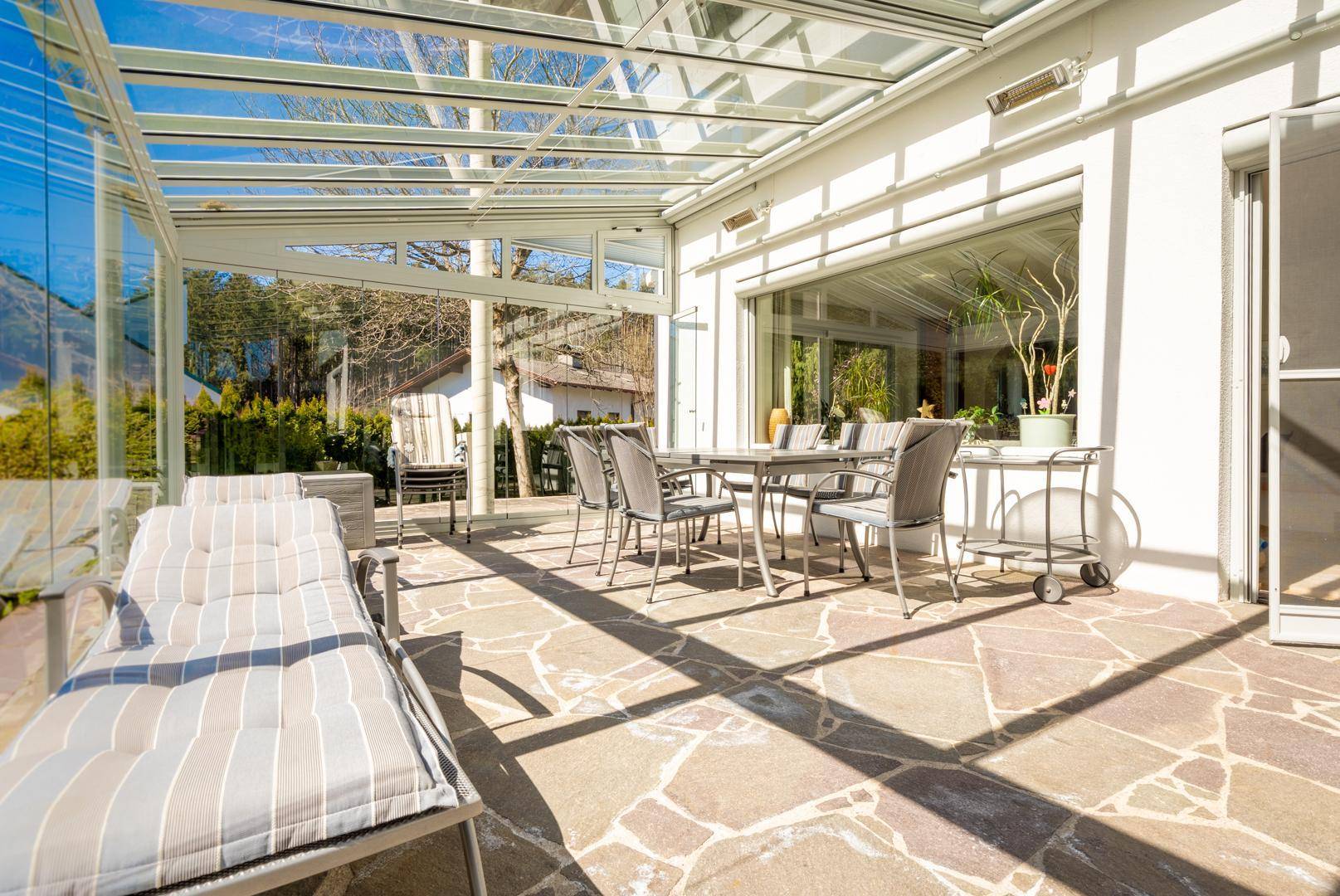 Verglaster Wintergarten mit Terrassenmöbeln und Liege, ideal für sonnige Stunden im Freien.