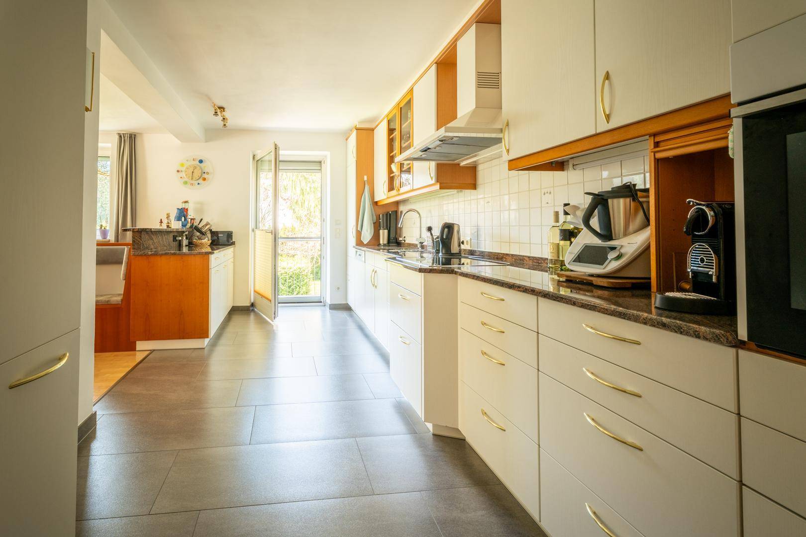 Helle Küche mit weißen Schränken, Holzdetails und dunkler Arbeitsplatte, führt zu einem Ausgang.