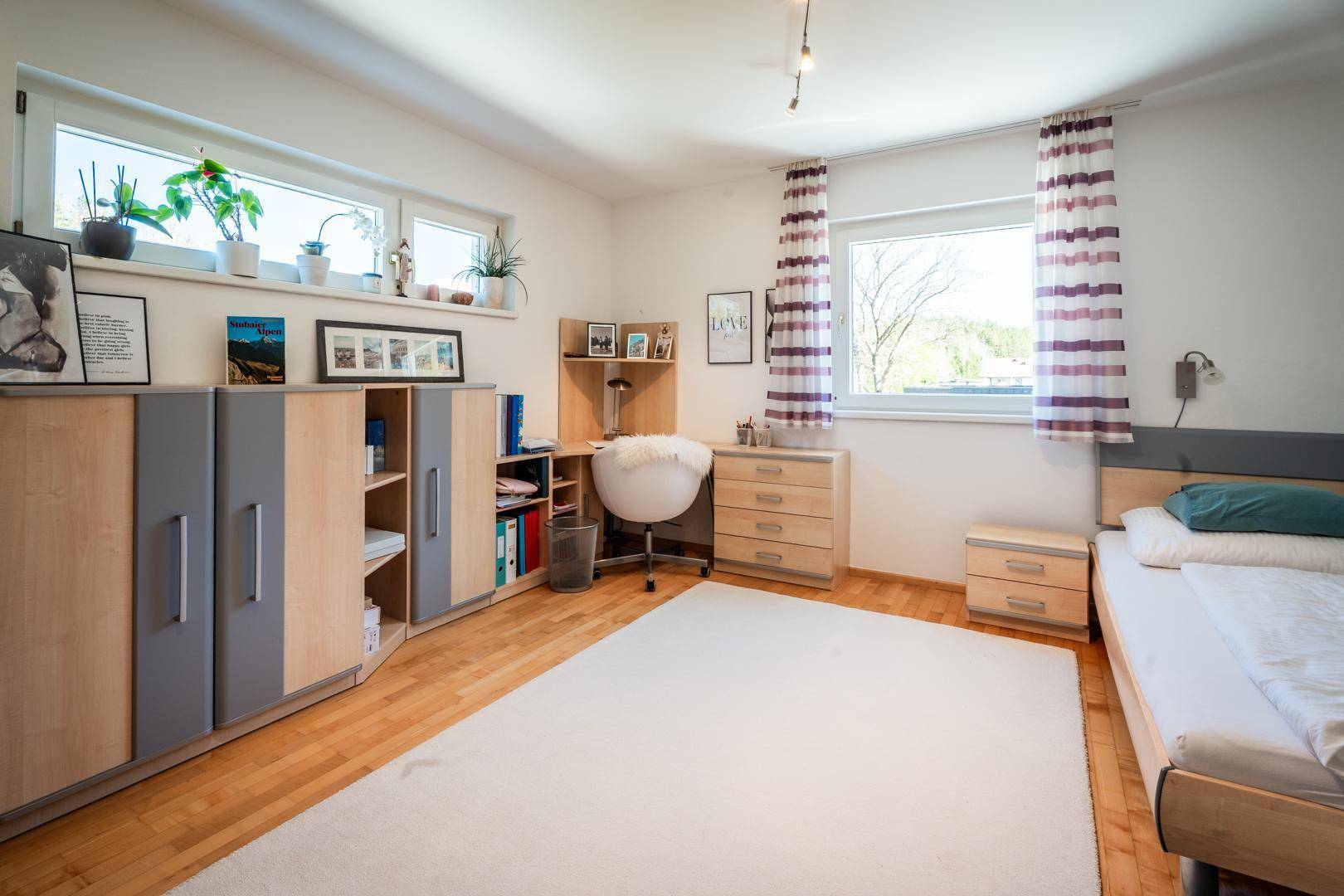 Schlafzimmer mit Schreibtischbereich, Holzboden und großen Fenstern, bietet viel Stauraum.