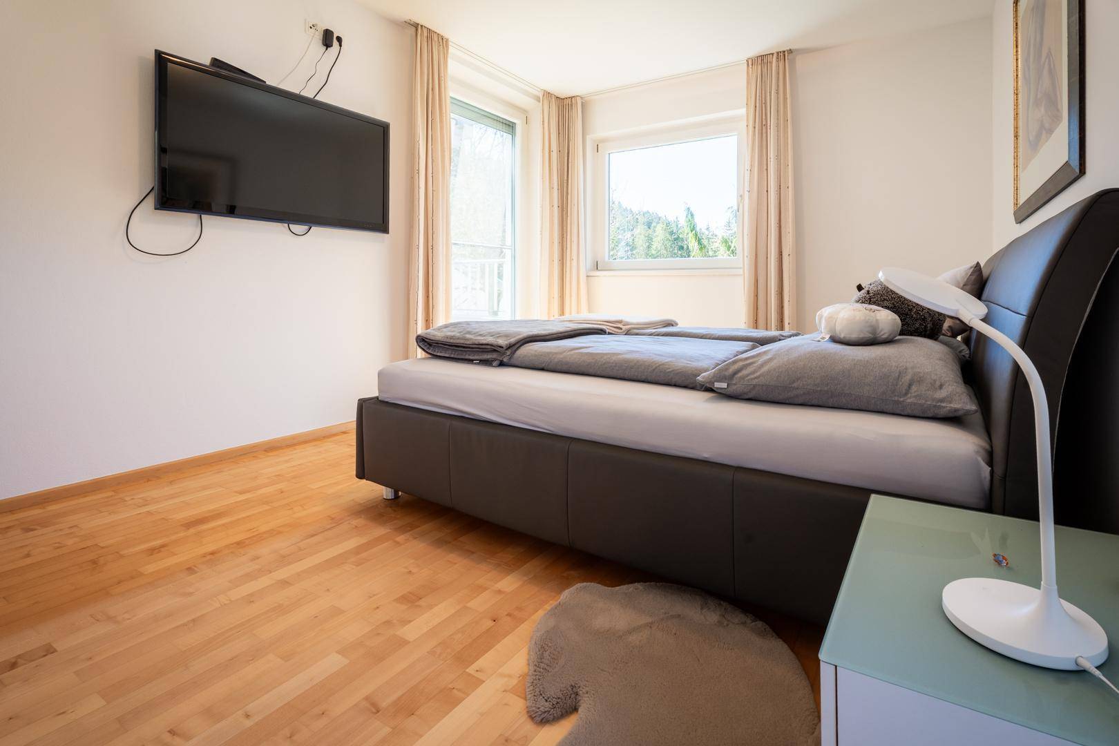 Modernes Schlafzimmer mit Doppelbett, Holzboden und großen Fenstern mit Blick ins Grüne.