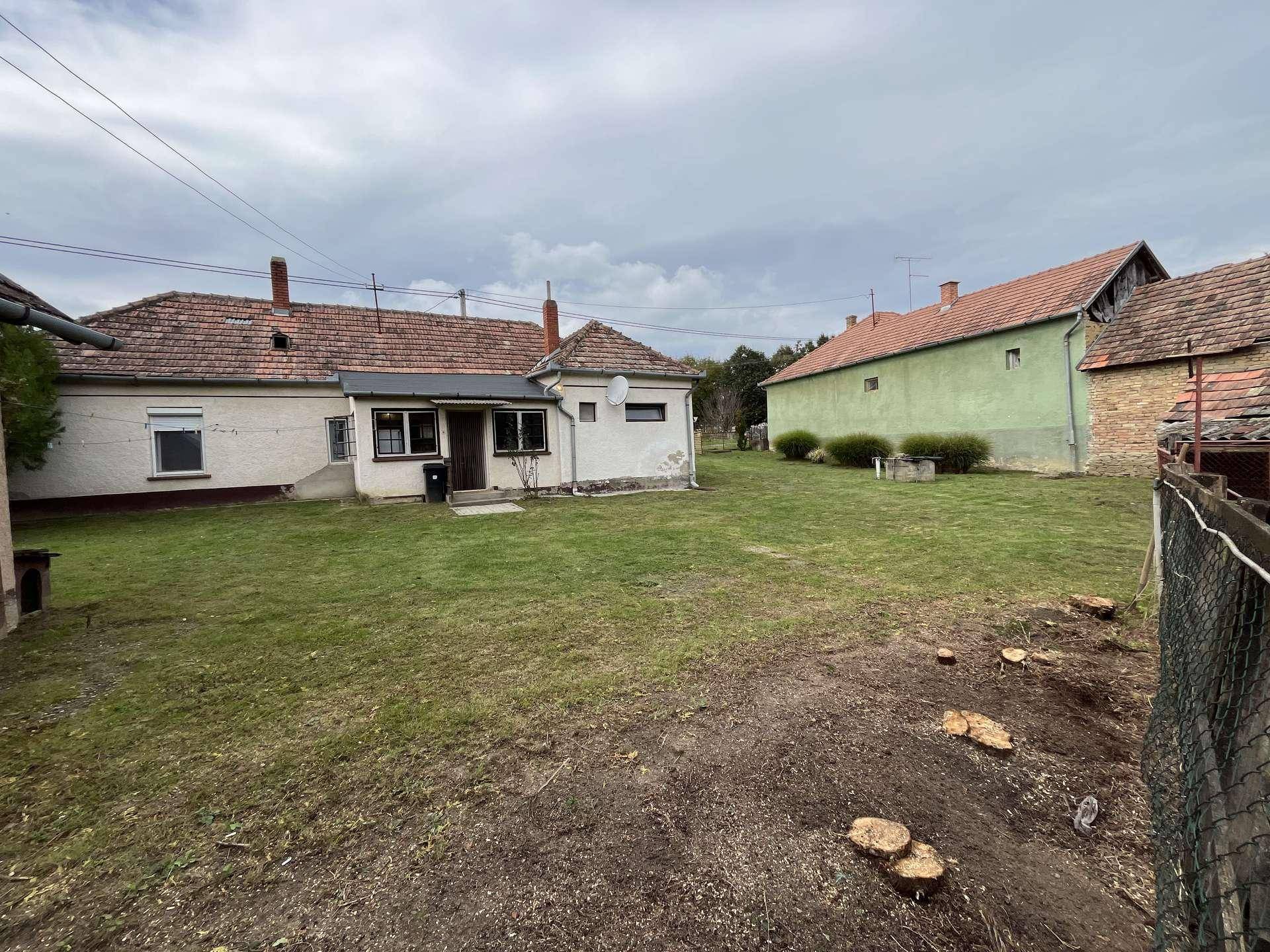 Hinterhofansicht des Hauses mit Rasenfläche und einigen Baumstümpfen, umgeben von ländlicher Bebauung.