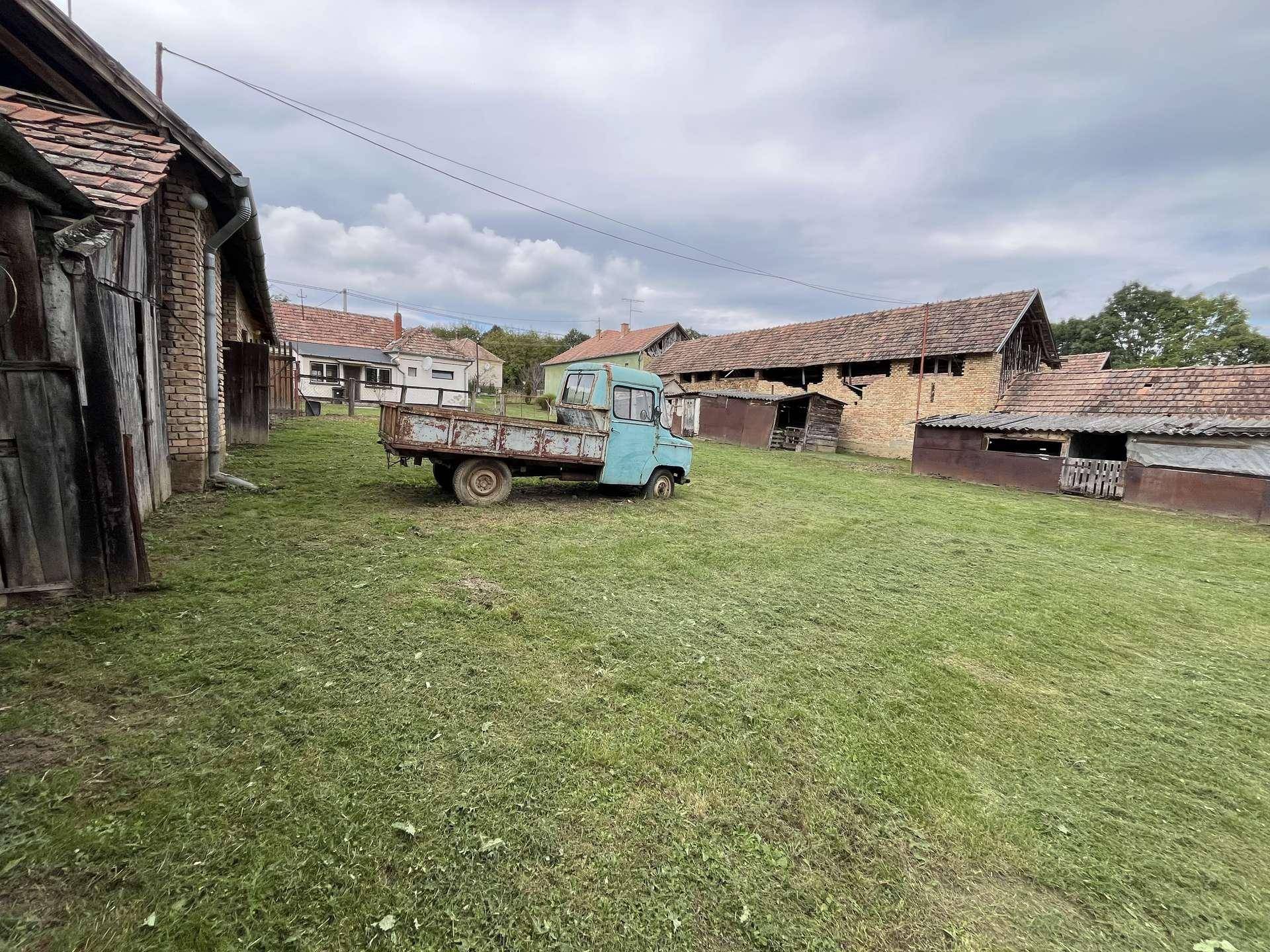 Ansicht des ländlichen Anwesens mit einem alten blauen Lastwagen und weiteren Bauerngebäuden im Hintergrund.
