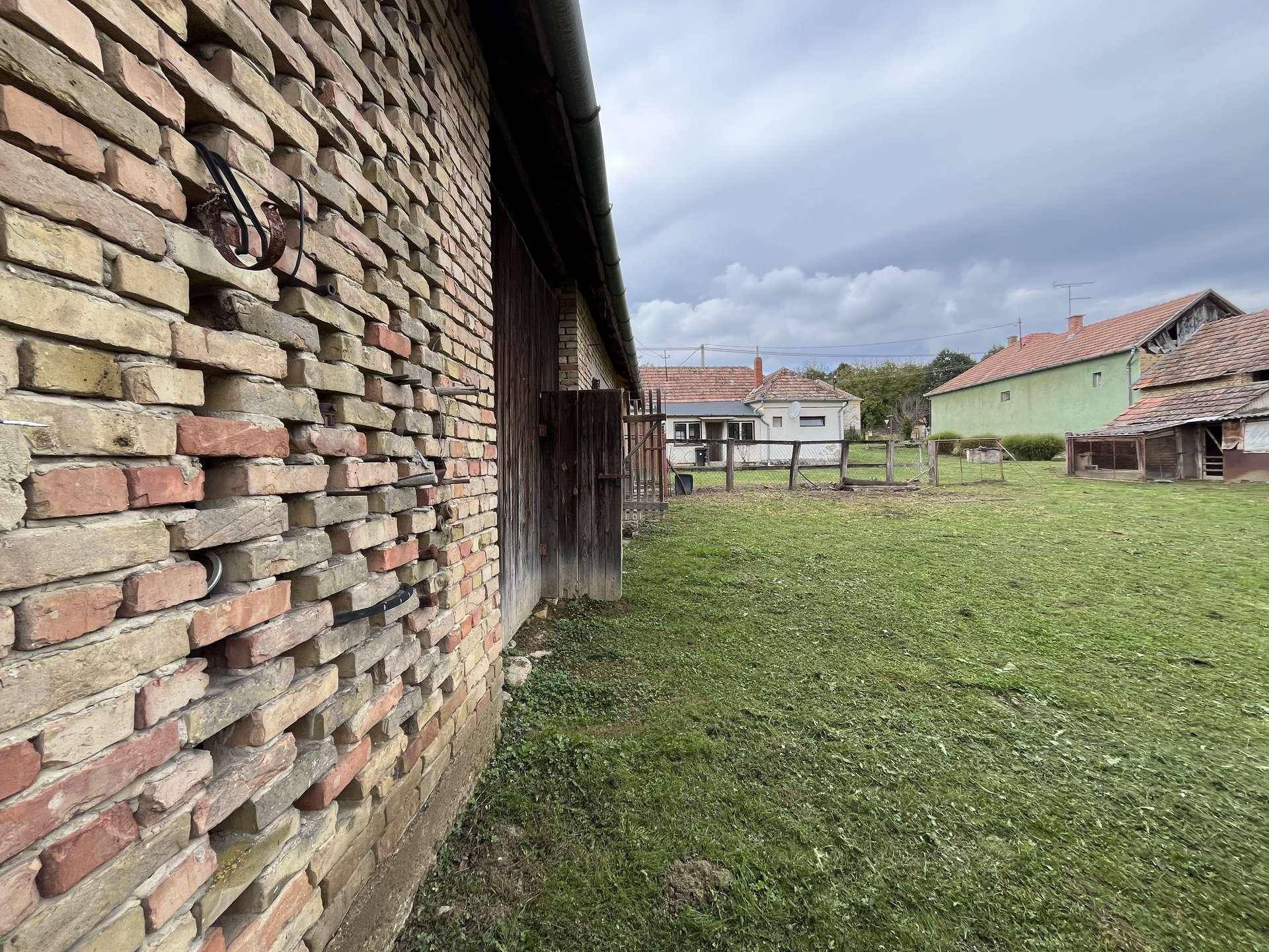 Detailansicht einer alten Ziegelmauer eines Bauerngebäudes mit einem weiten Rasenbereich im Hintergrund.