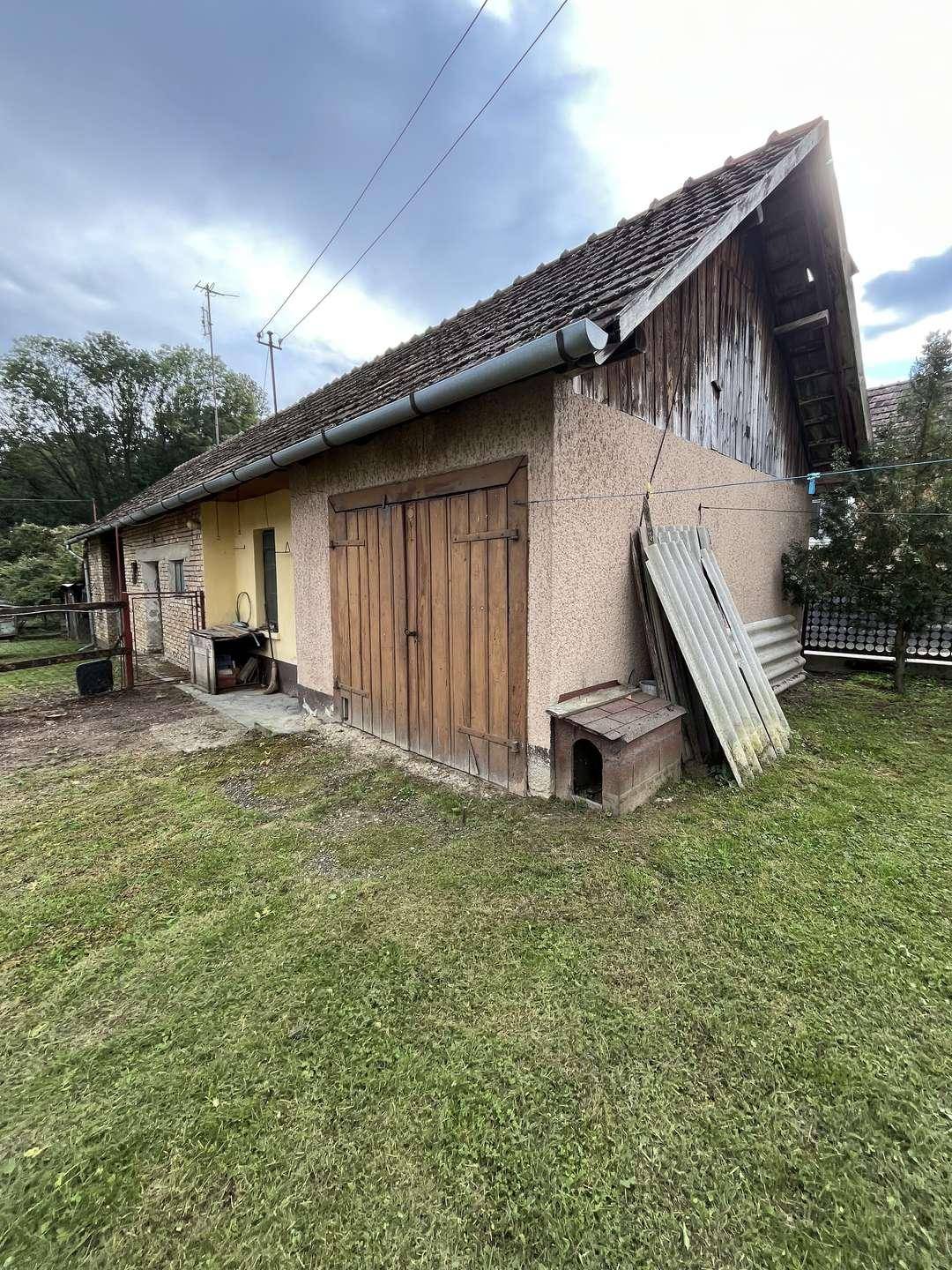 Außenansicht eines Nebengebäudes mit Holztor, einem Hundehäuschen und einem schrägen Dach.