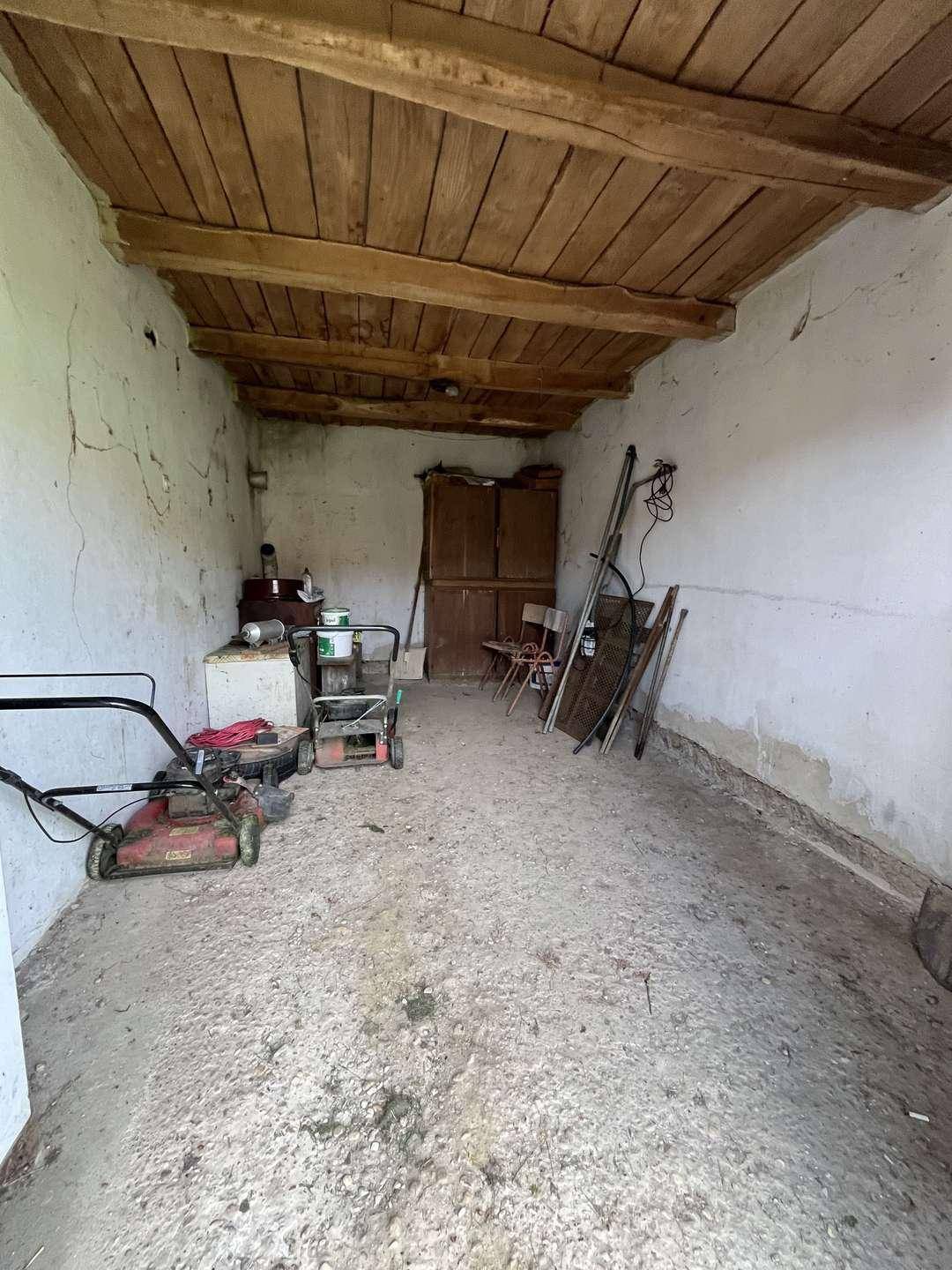 Einfacher Abstellraum mit Betonboden, Holzdecke und Gartengeräten, ideal für Lagerzwecke.