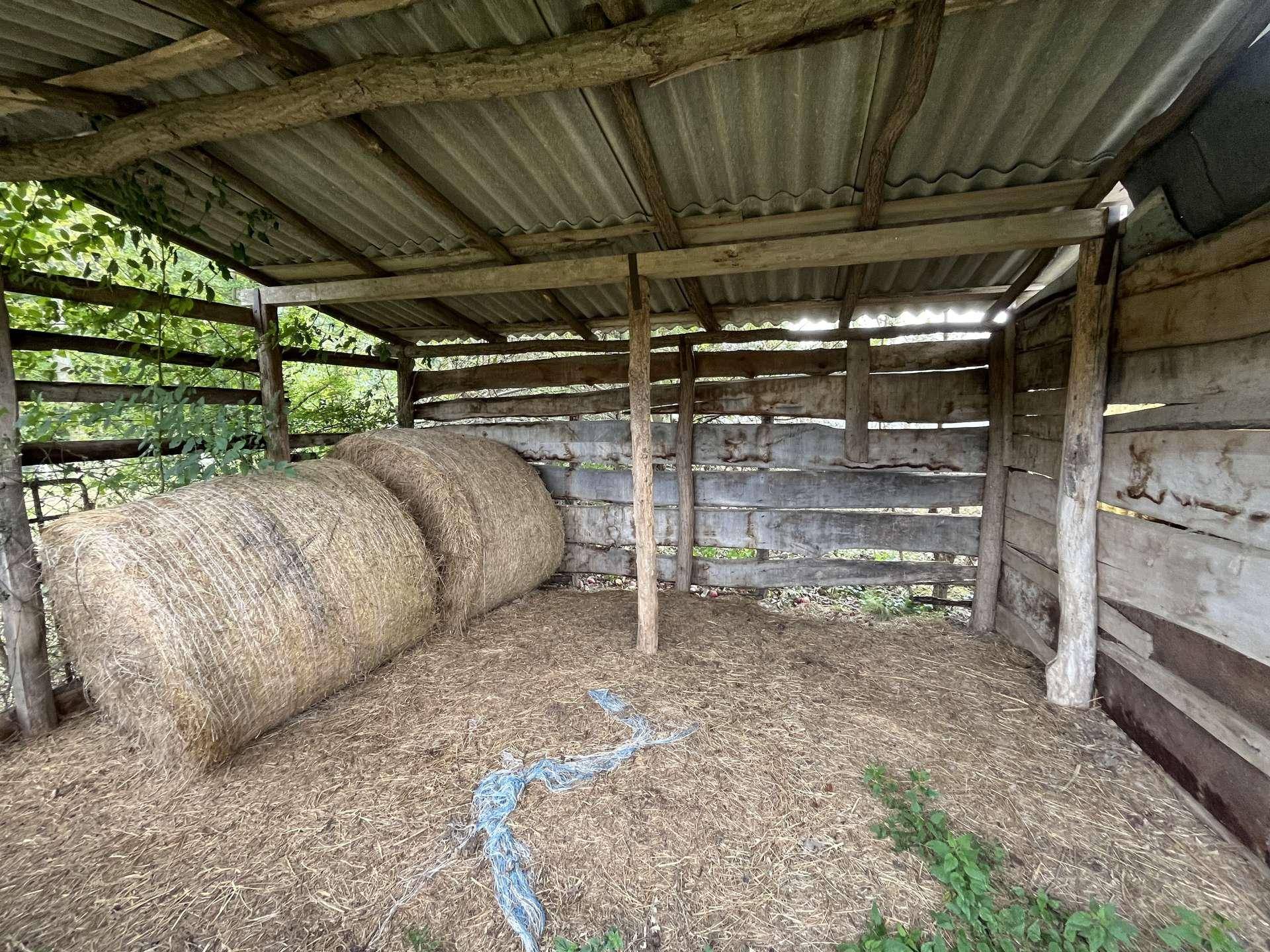 Innenansicht eines weiteren Schuppenbereichs mit großen Heuballen und einfacher Holzkonstruktion.