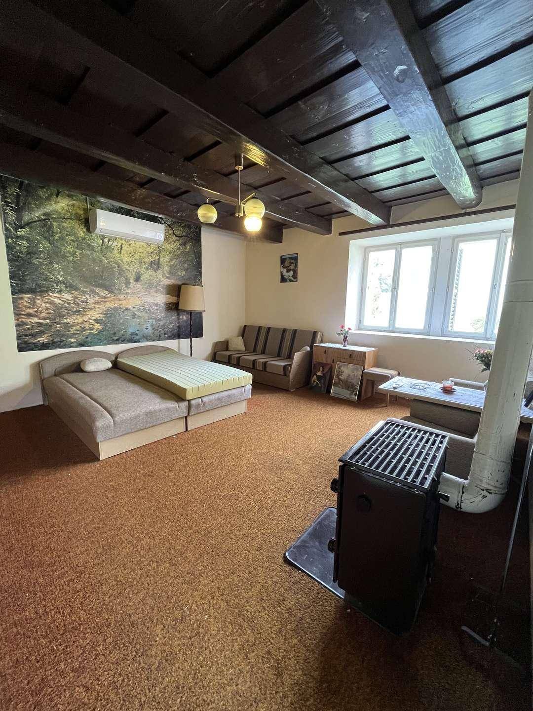 Geräumiges Wohnzimmer mit Holzbalkendecke, Kaminofen und rustikalem Teppichboden.