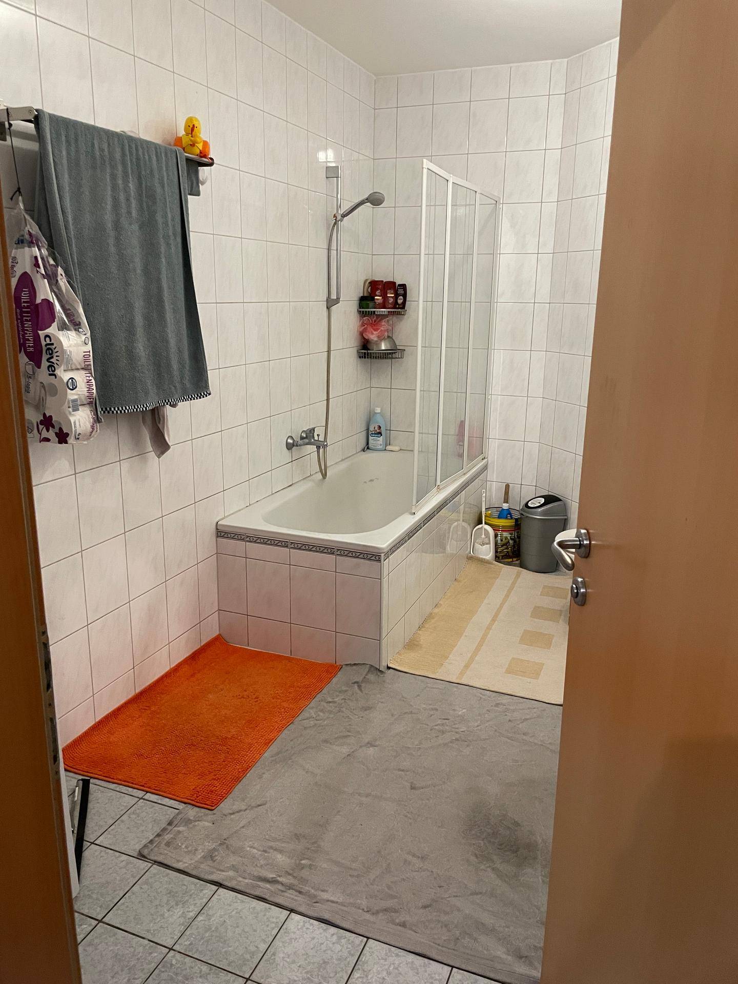Badezimmer mit Badewanne, Duschabtrennung und hellen, weiß gefliesten Wänden und Boden.