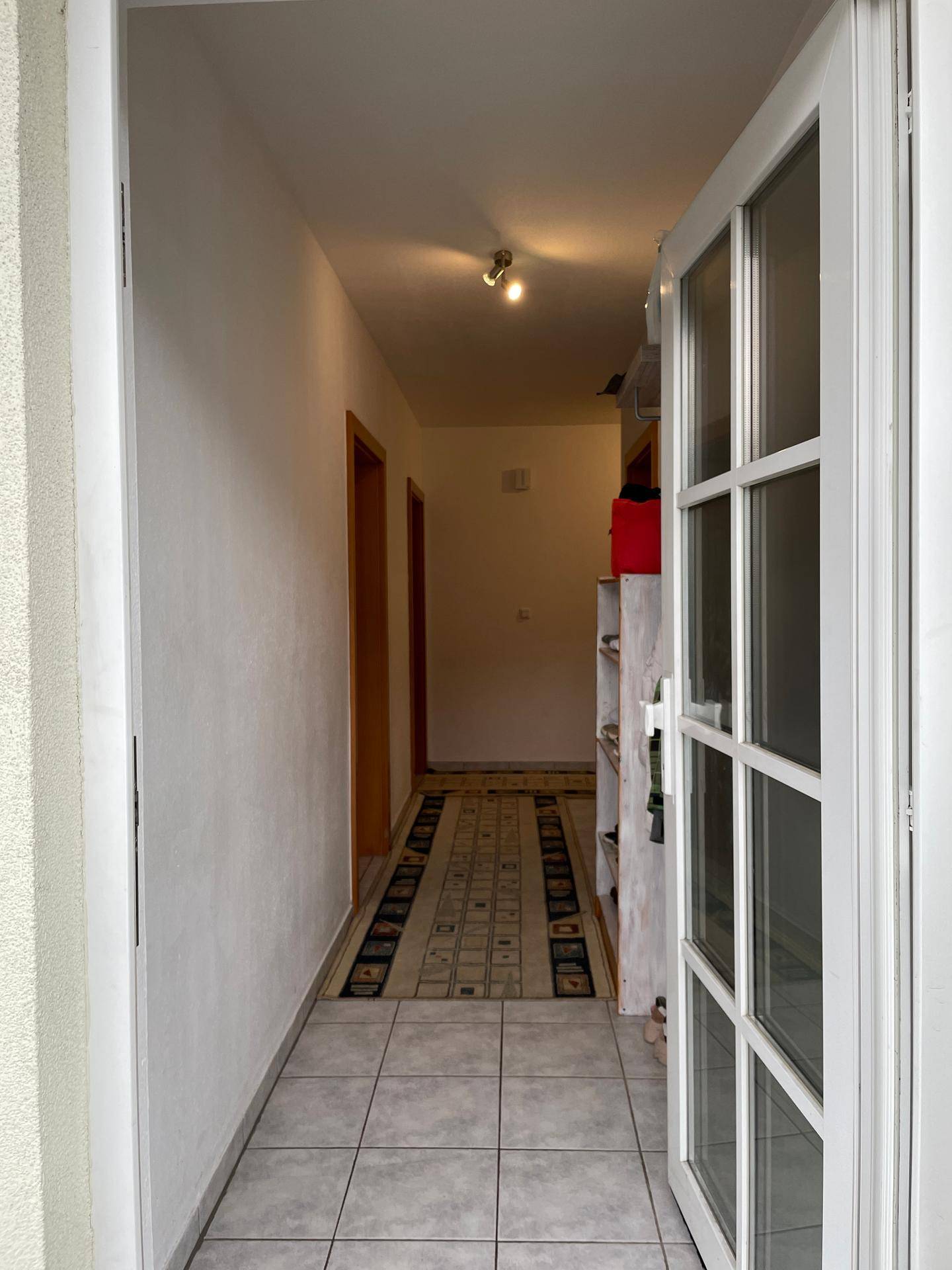Heller Eingangsbereich mit Fliesenboden und einem gemusterten Teppichläufer, der in den Innenraum führt.