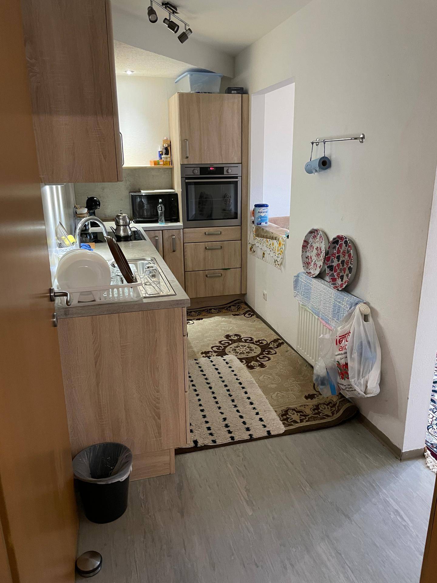 Funktionale Küche mit hellen Holzschränken, Einbaugeräten und einem Teppichläufer auf dem Boden.