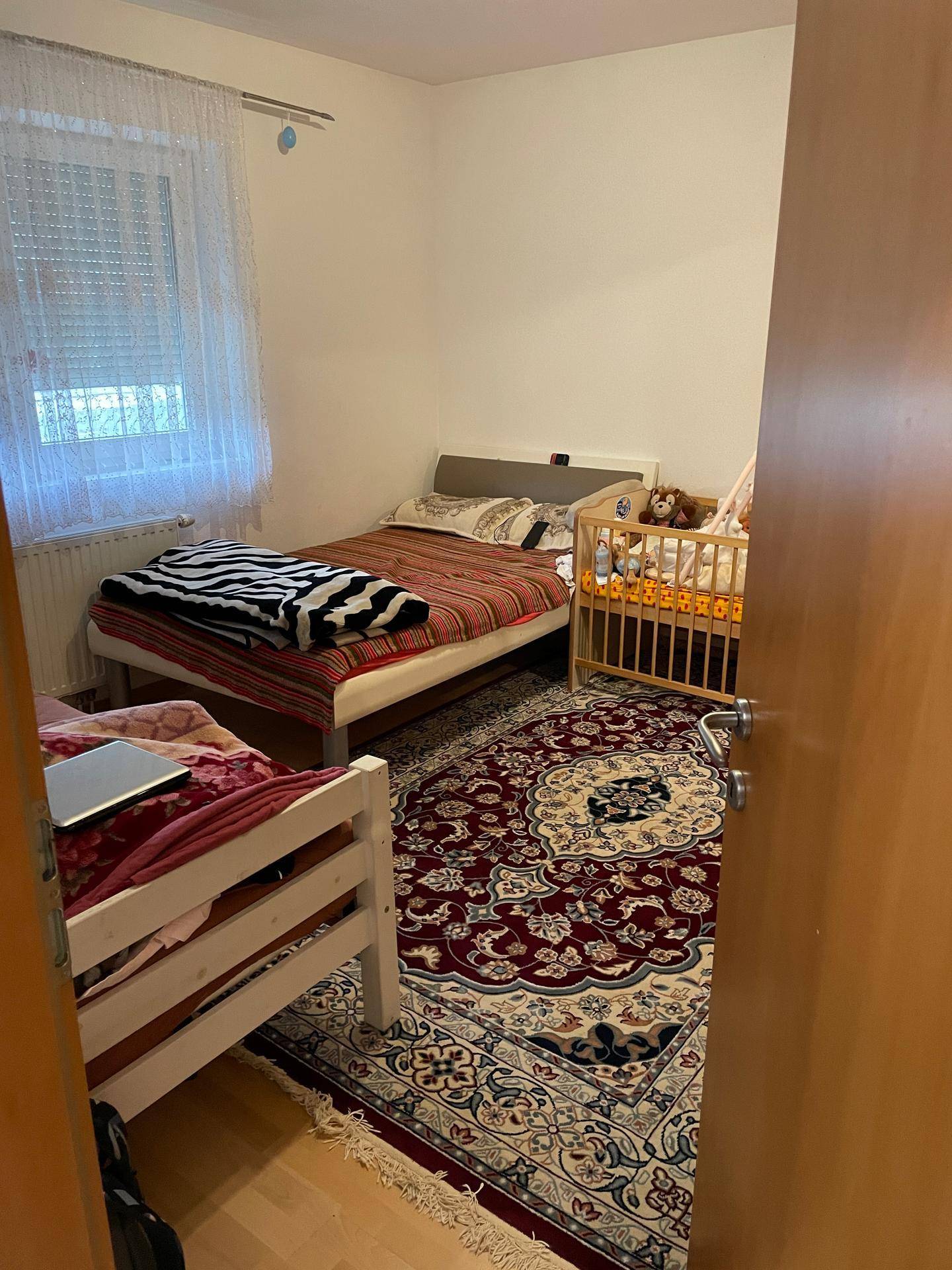 Gemütliches Schlafzimmer mit zwei Einzelbetten, einem Babybett und einem großen, traditionellen Teppich.