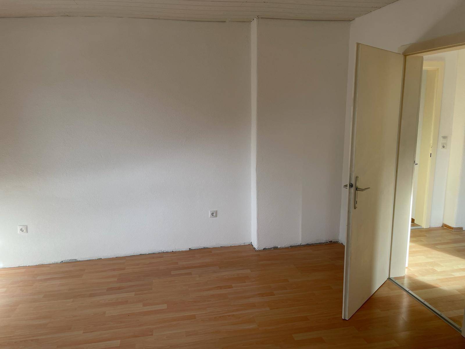 Leeres Schlafzimmer mit Laminatboden und weißen Wänden, bereit zur individuellen Gestaltung.