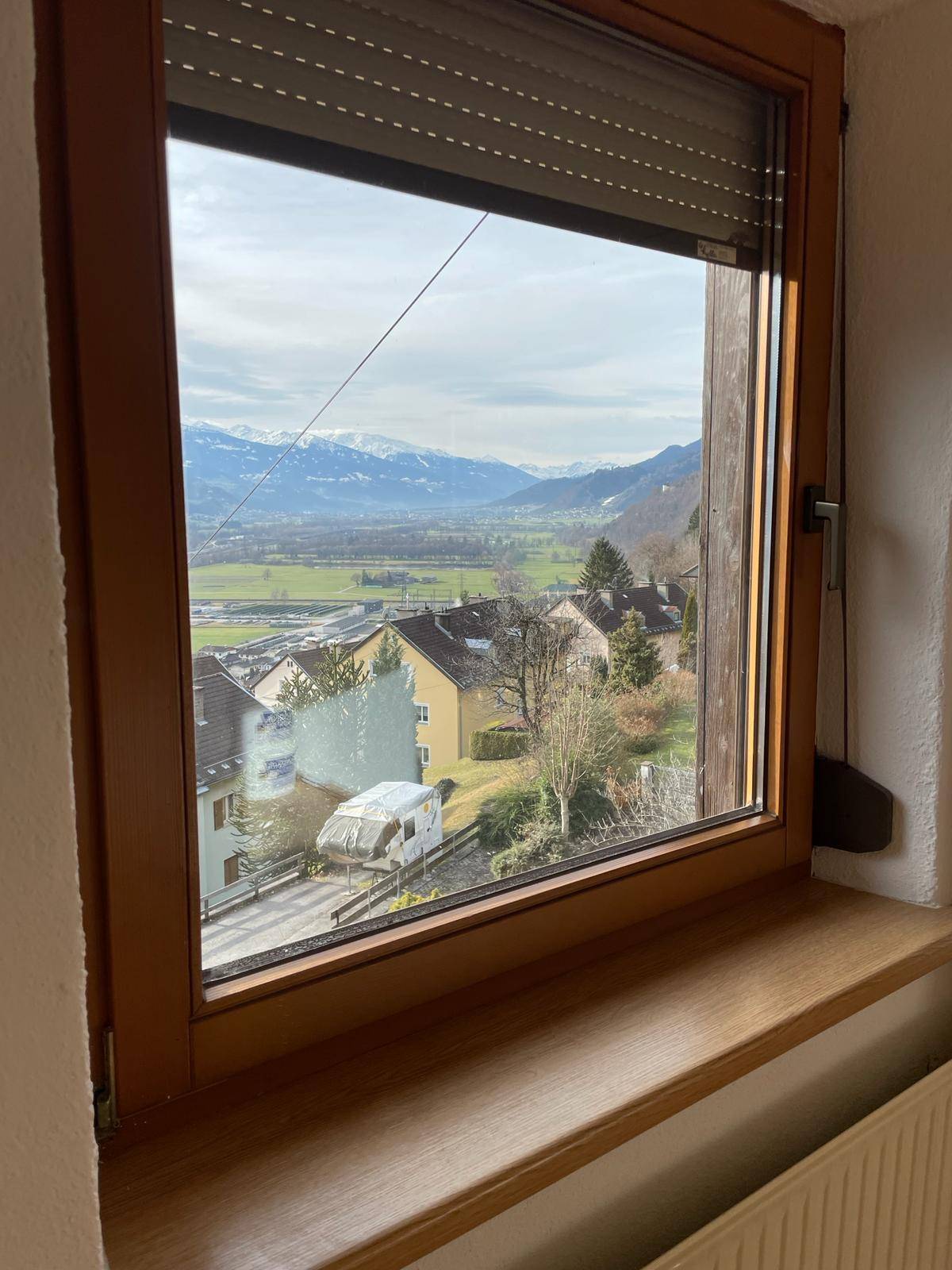 Fensterblick auf die malerische Berglandschaft und das darunterliegende Tal mit Häusern.