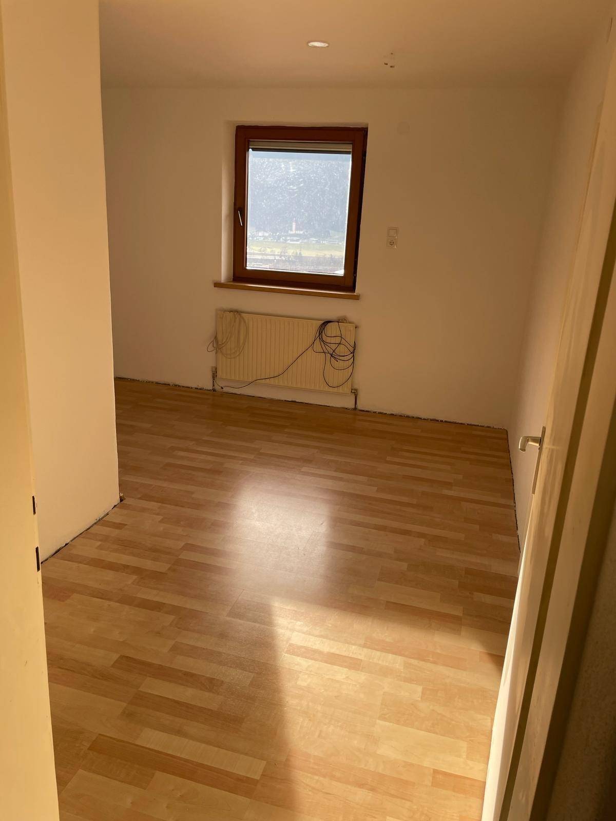 Helles Schlafzimmer mit Laminatboden, weißen Wänden und einem Fenster mit Bergblick.