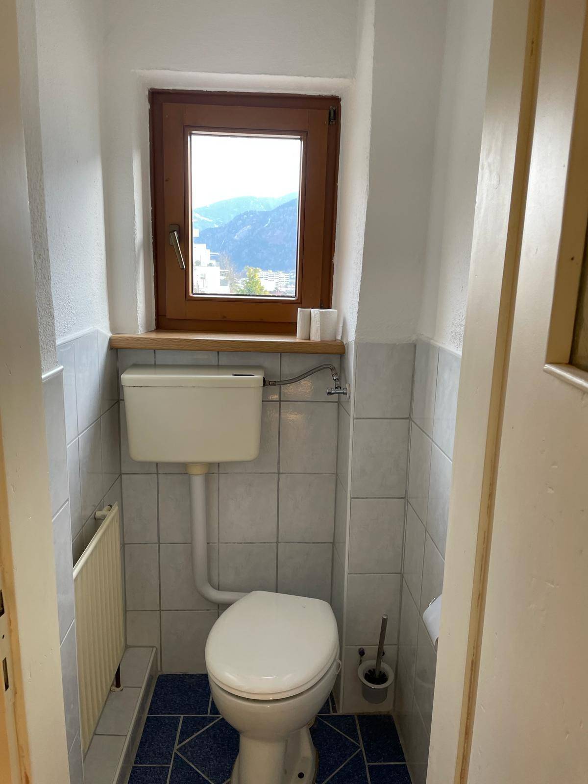 Kleines Gäste-WC mit Fenster, WC, Waschbecken und blau-weißen Fliesen.