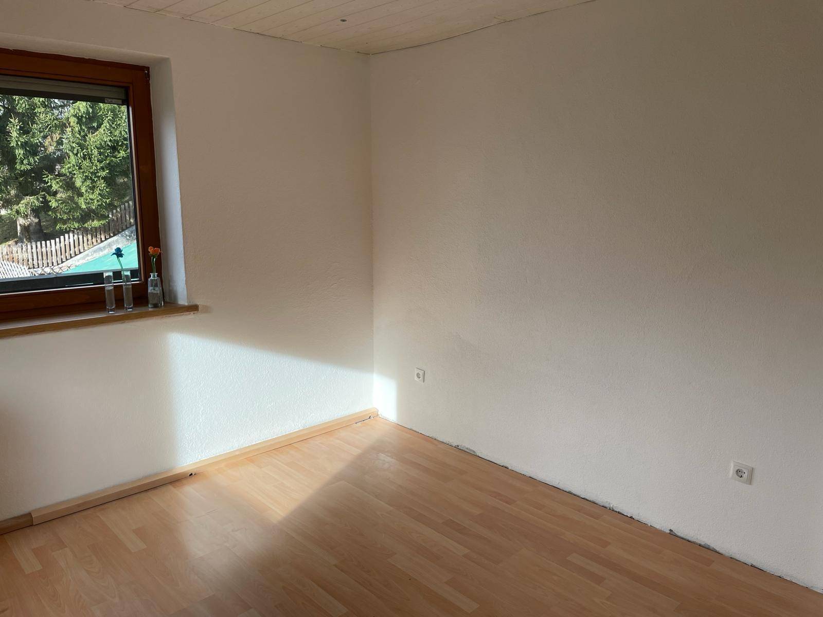 Helles Zimmer mit Laminatboden und Blick auf Bäume und einen Pool im Außenbereich.