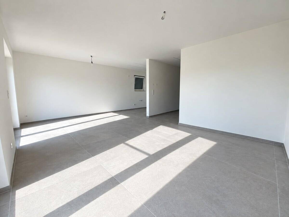 Heller, leerer Wohnbereich mit modernen grauen Fliesen und viel Tageslicht.