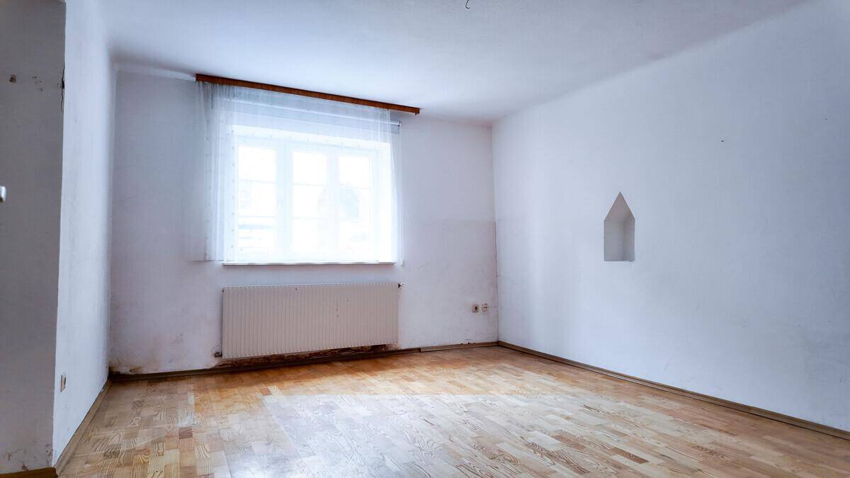 Leerer Raum mit Parkettboden, einem Fenster und einem Heizkörper unter der Fensterbank.