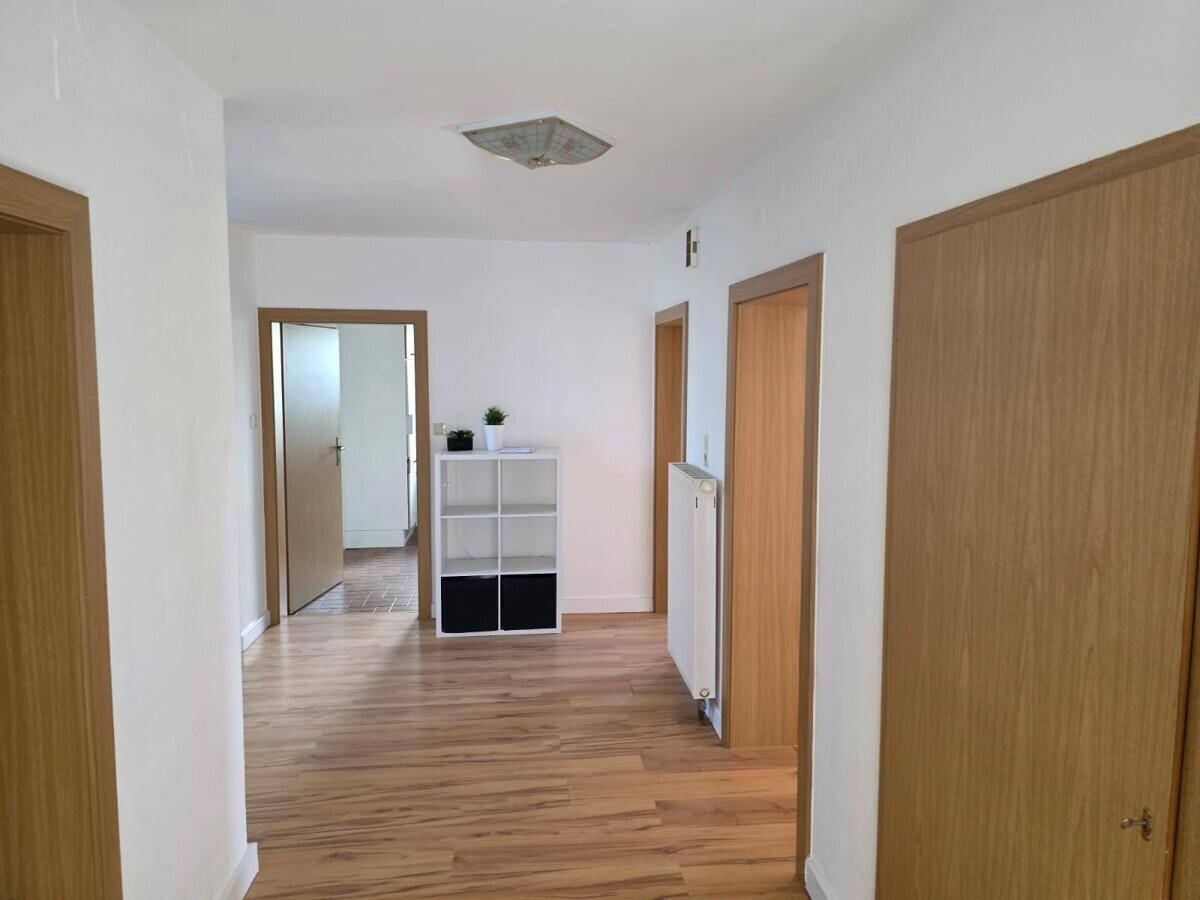 Heller Flur mit Laminatboden, weißen Wänden und Holztüren, der zu weiteren Räumen führt.