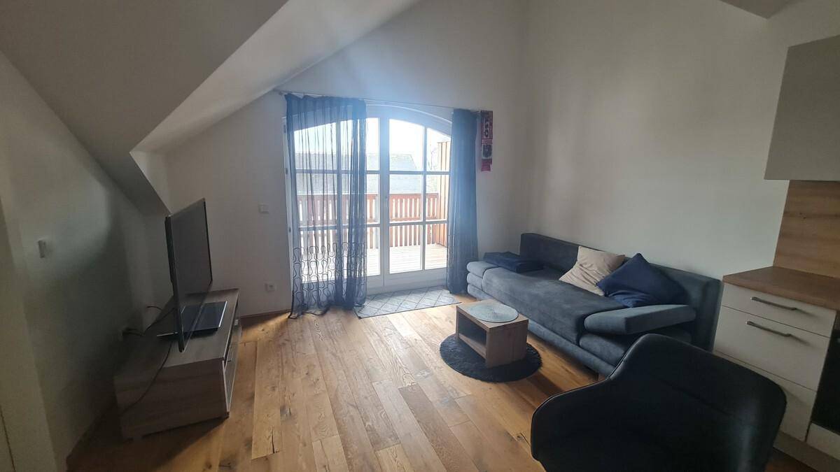 Heller Wohnbereich mit Holzboden, Dachschrägen und Zugang zu einem Balkon.