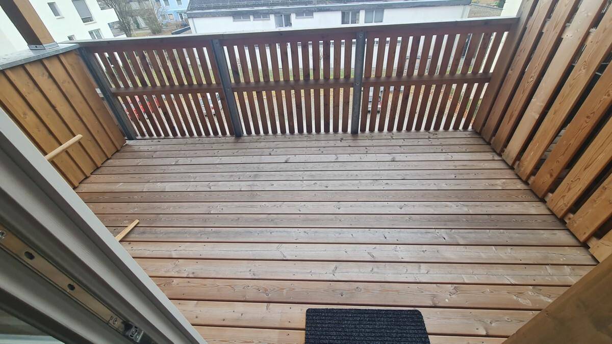 Geräumiger Holzbalkon mit Holzgeländer und Blick auf die Umgebung.