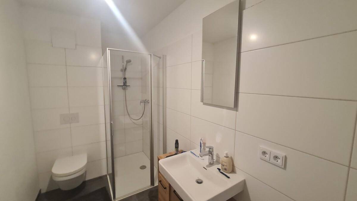 Modernes Badezimmer mit weißen Fliesen, Dusche und wandhängendem WC.