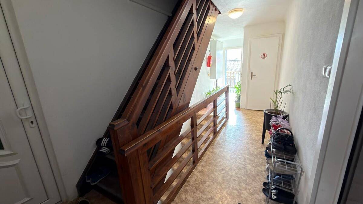 Flur mit Holztreppe und Blick in einen hellen Bereich mit Zugang zu einem Balkon.