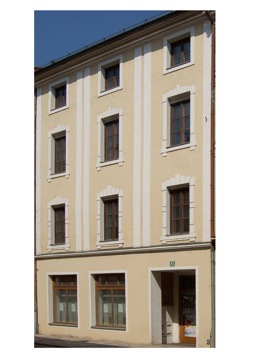 Historische Fassade eines Mehrfamilienhauses mit traditionellen Fenstern und Putzgliederung.