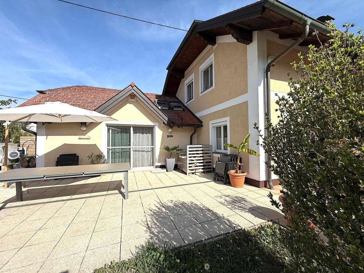 Gepflasterte Terrasse mit Sonnenschirm und Esstisch, ideal für Mahlzeiten im Freien.