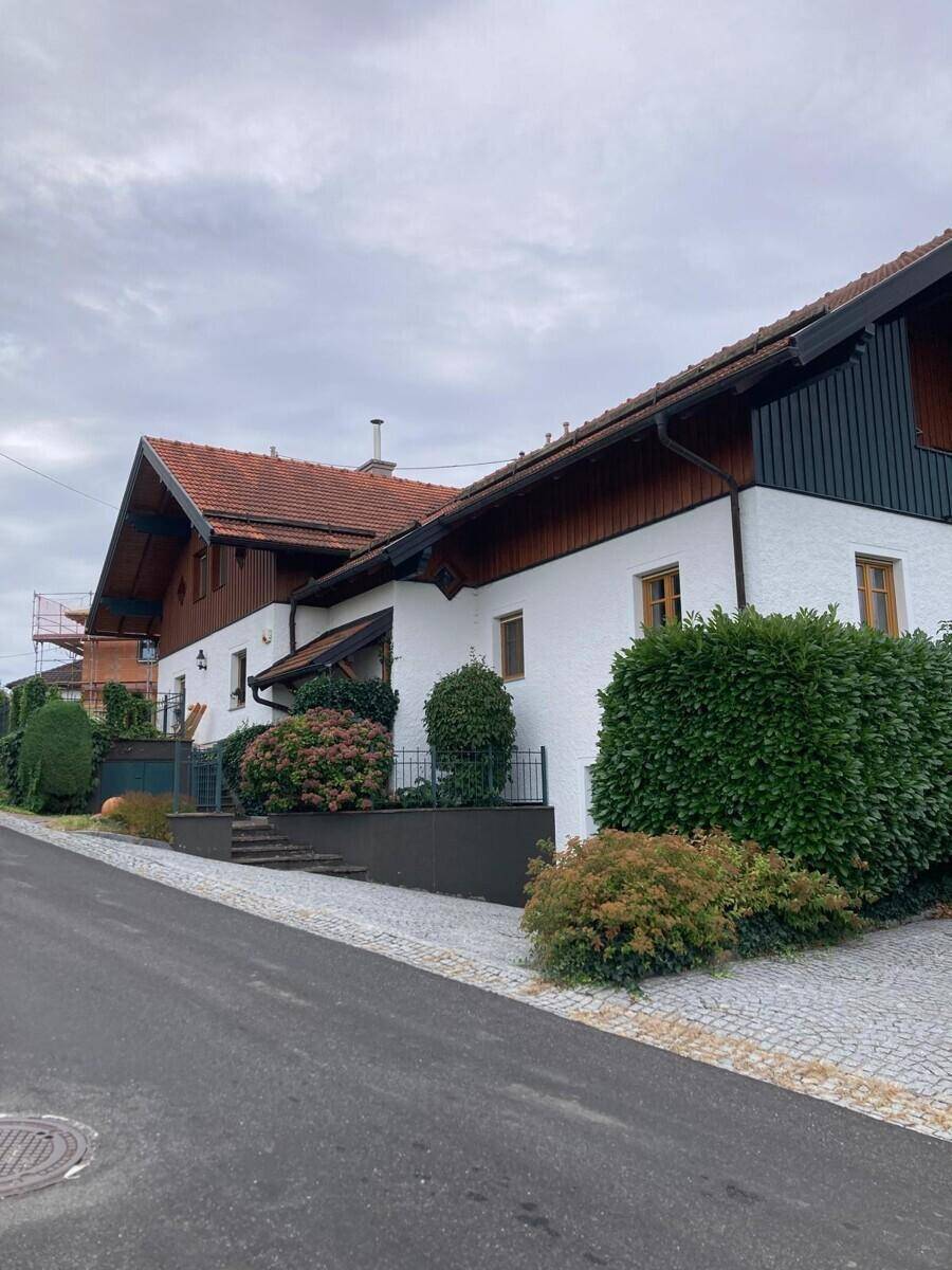 Traditionelle Hausfassade mit weißem Putz, Holzelementen und gepflasterter Zufahrt.