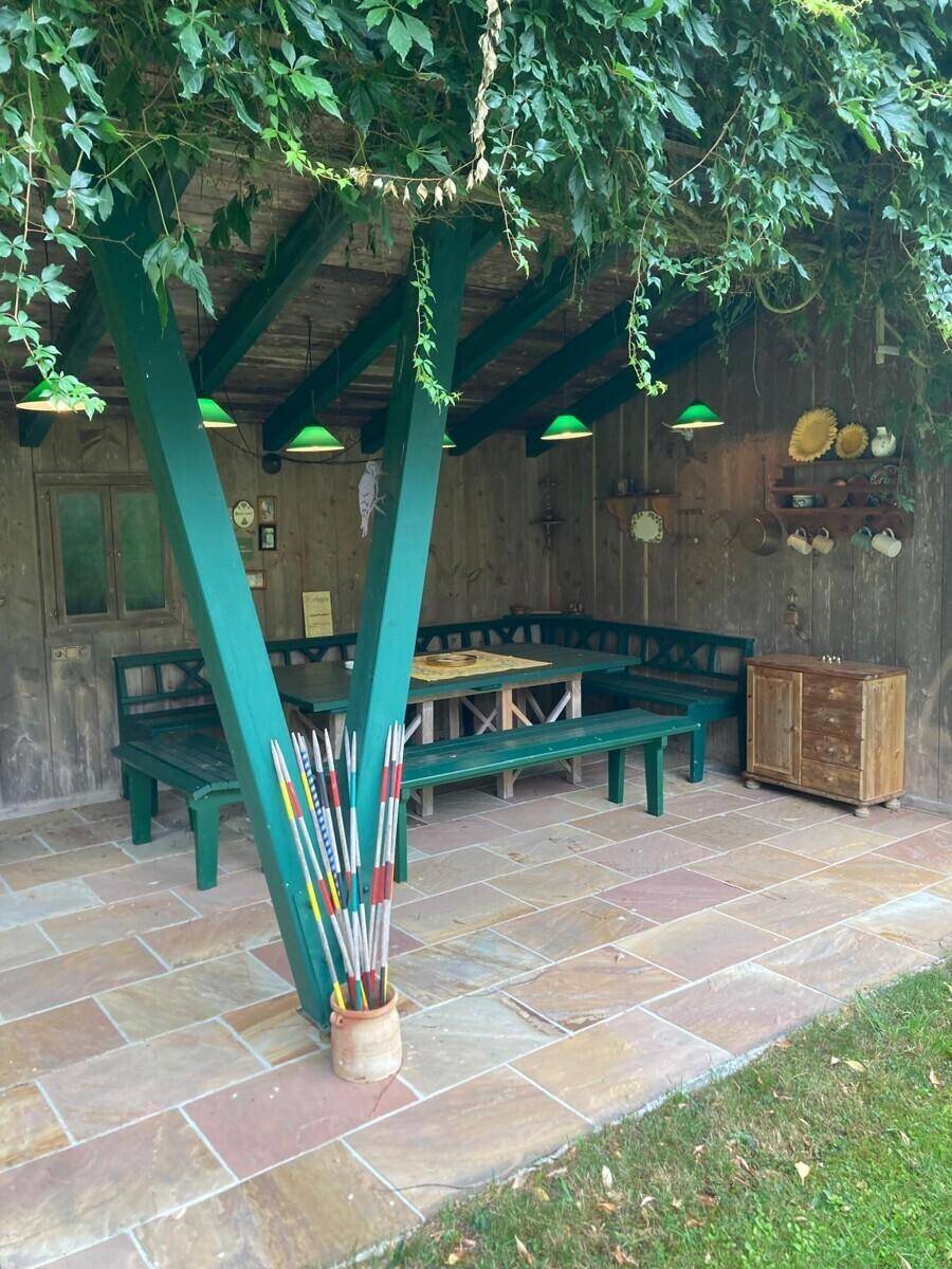 Überdachter Außenbereich mit Holzbänken, Tisch und Kletterpflanzen an der Pergola.