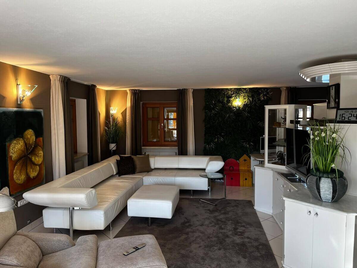Helles Wohnzimmer mit großer weißer Eckcouch, Teppich und dekorativer Wandbegrünung.