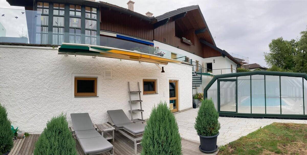 Außenbereich mit überdachtem Pool, Liegestühlen und Zugang zum Gebäude.