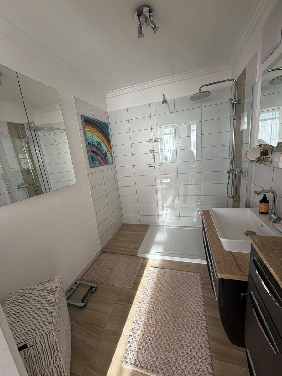 Modernes Badezimmer mit begehbarer Dusche, weißen Fliesen und Holzoptikboden.