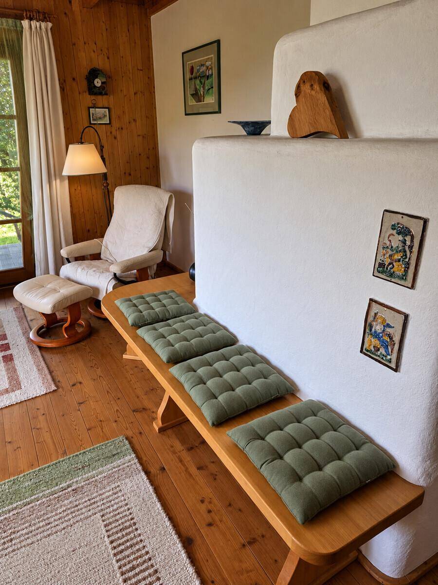 Gemütliches Wohnzimmer mit Holzboden, Kachelofen und bequemer Sitzbank in rustikalem Stil.