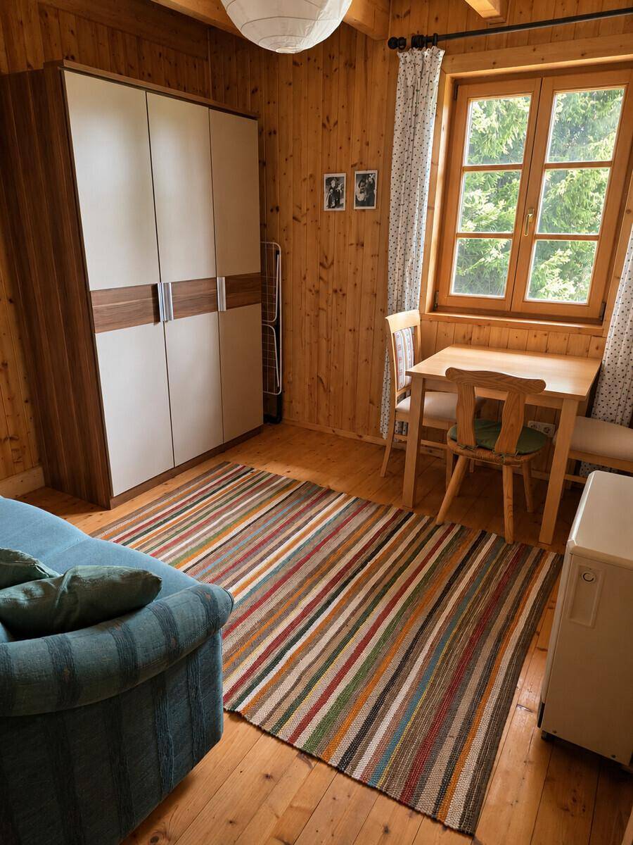 Schlafzimmer mit Holzvertäfelung, Kleiderschrank und kleinem Esstisch am Fenster, hell und einladend.