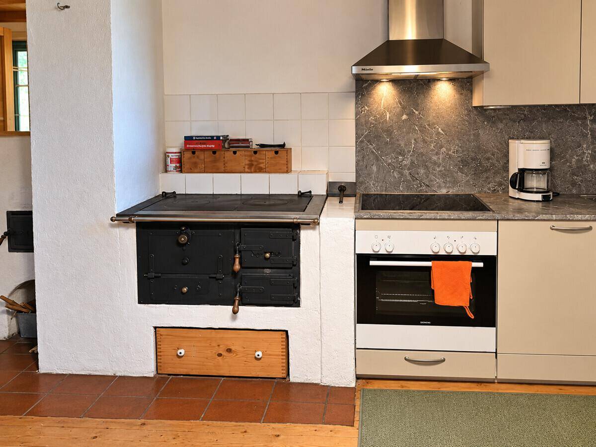 Rustikale Küche mit traditionellem Holzofen, modernem Herd und Dunstabzugshaube, funktional und gemütlich.
