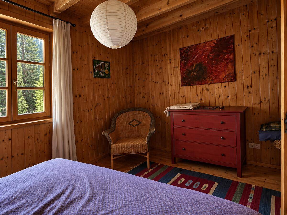 Gemütliches Schlafzimmer mit Holzwänden, Holzboden und einem Fenster mit Blick ins Grüne, sehr hell.