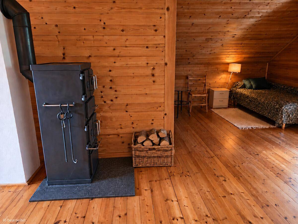 Rustikaler Dachboden mit Holzofen, Holzboden und einem Schlafbereich im Hintergrund, sehr gemütlich.
