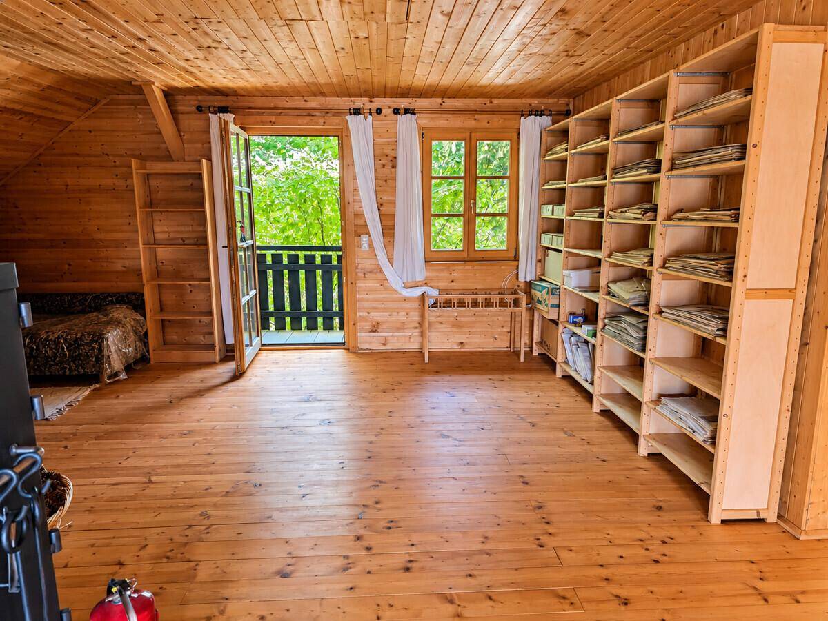 Geräumiger Dachboden mit Holzboden, Bücherregalen und Zugang zu einem kleinen Balkon, lichtdurchflutet.