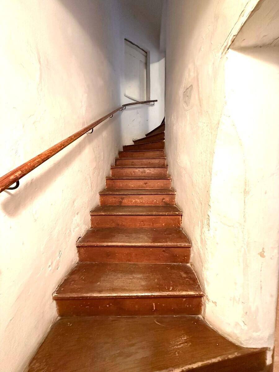 Schmale Holztreppe mit Handlauf, die in einem historischen Gebäude nach oben führt.
