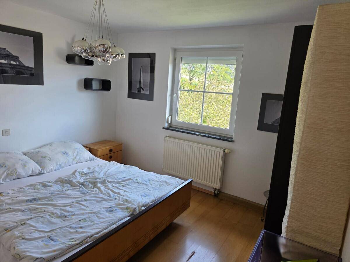Schlafzimmer mit Holzbett, Nachttischen und einem Fenster mit Blick ins Grüne.