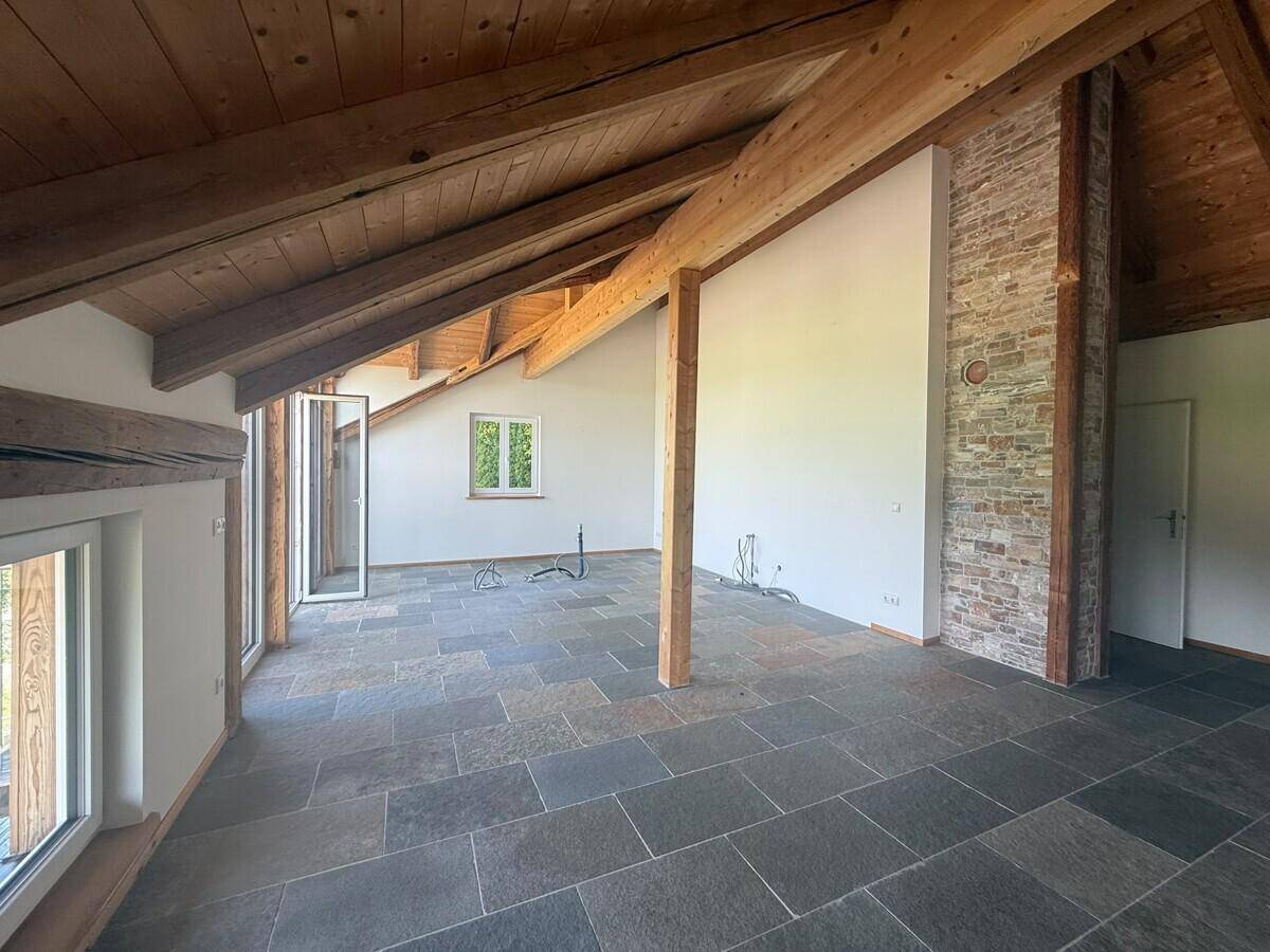 Geräumiger Wohnbereich mit hoher Holzbalkendecke, Schieferboden und Ziegelakzenten.