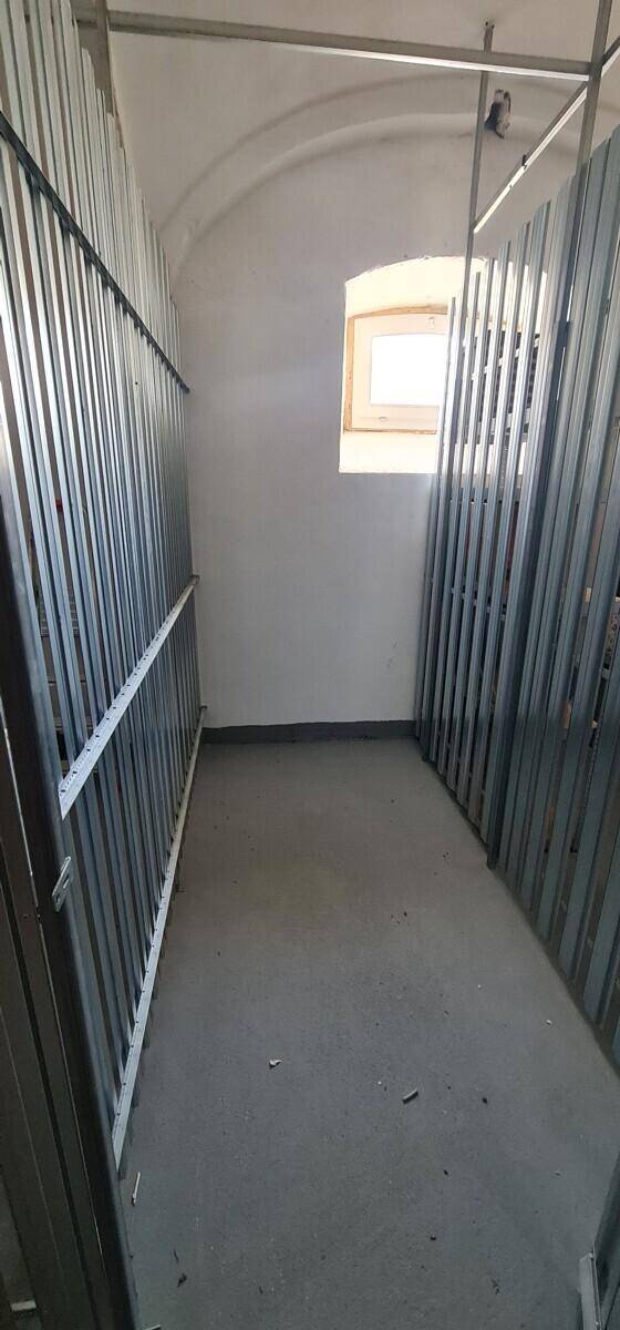 Funktionaler Abstellraum im Keller mit Metallabtrennungen und kleinem Fenster für Tageslicht.