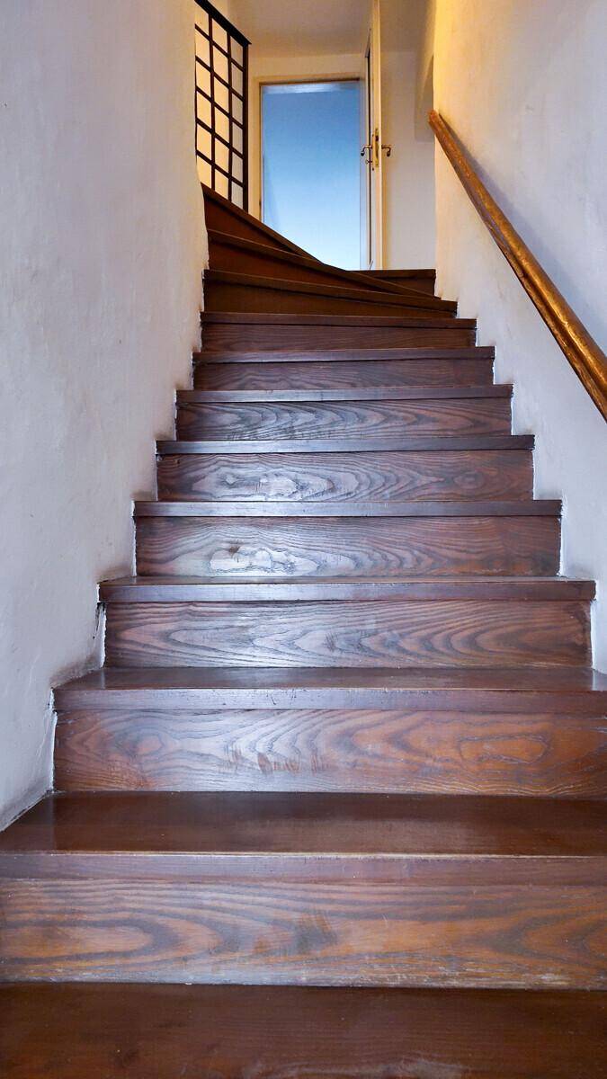 Dunkle Holztreppe mit sichtbarer Maserung, die zu den oberen Stockwerken des Gebäudes führt.